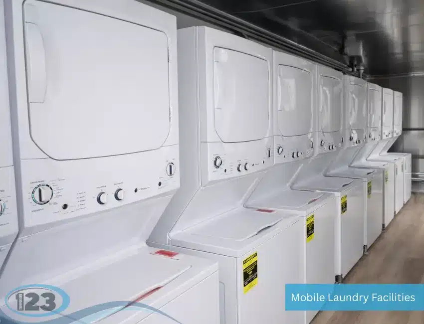A rows of white commercial laundry machines stacked inside a portable, well-lit mobile laundry unit.